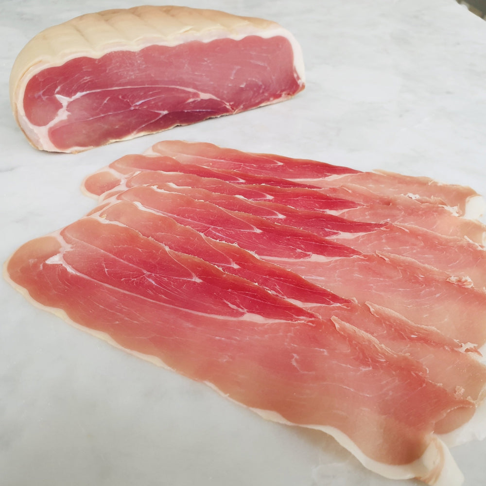A half piece of Papandrea Boneless Prosciutto with slices on a marble bench.